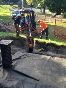 Paul and Manuel help guide the backhoe driver while trenching for the gravity-fed outlet that will be available for watering trees and gardens in the lower level of the park.